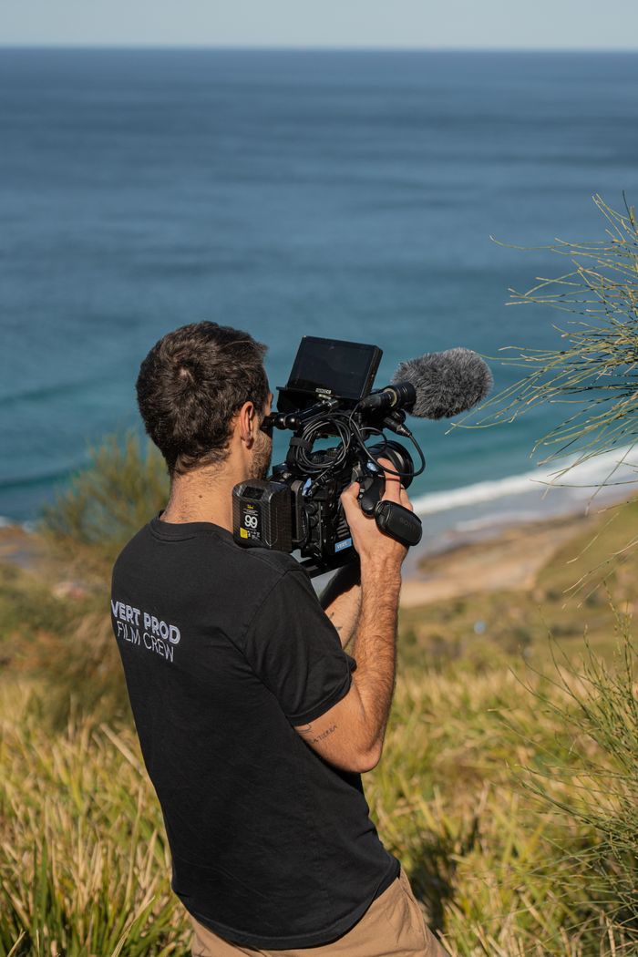 Filmmaker with camera capturing a scenic ocean view in Sydney, Australia.