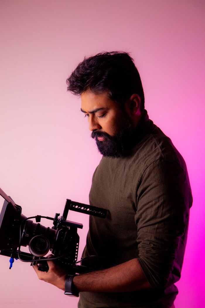 A bearded man in a green shirt holding a professional camera in a studio setting.