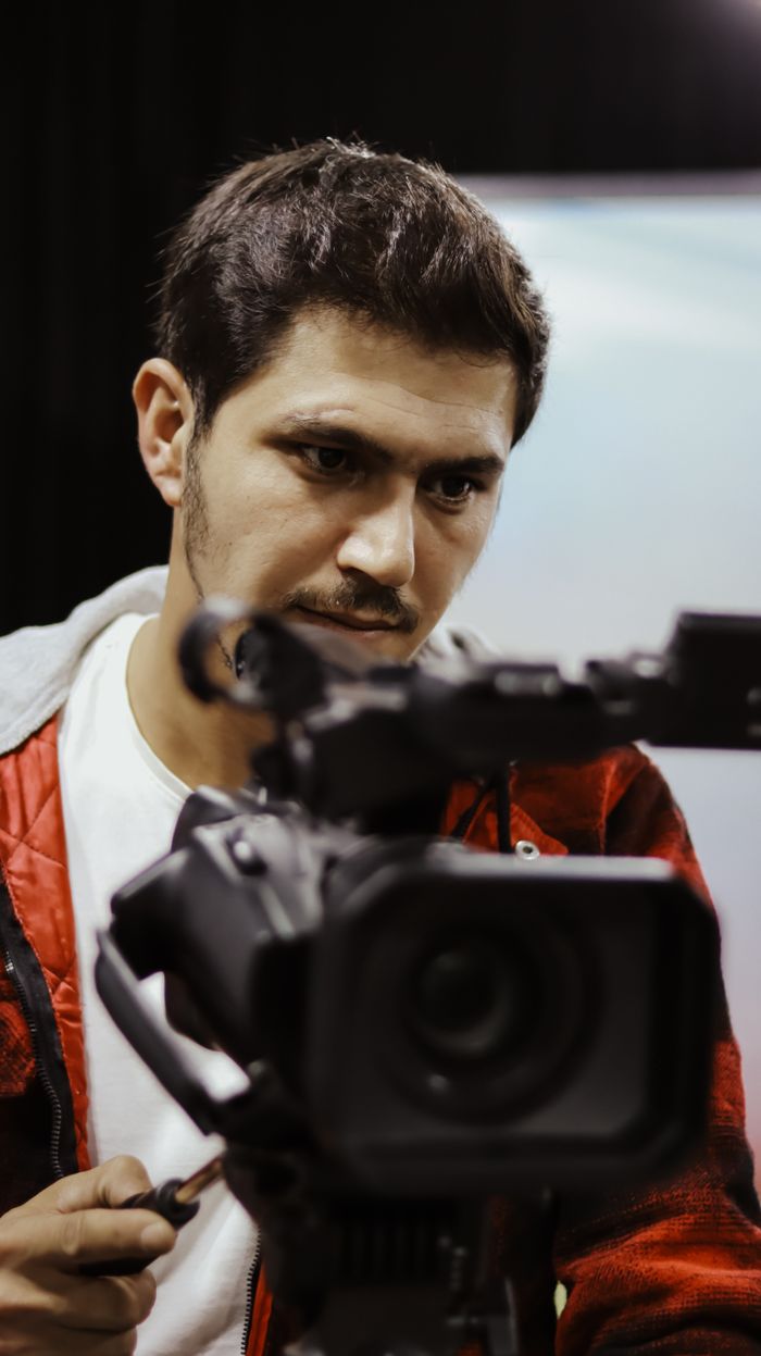 services-img Cameraman with short black hair operates a professional video camera indoors.