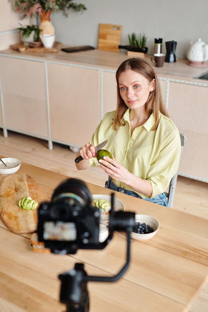 services-04 Caucasian woman filming herself peeling an avocado for a cooking vlog in a modern kitchen setting.