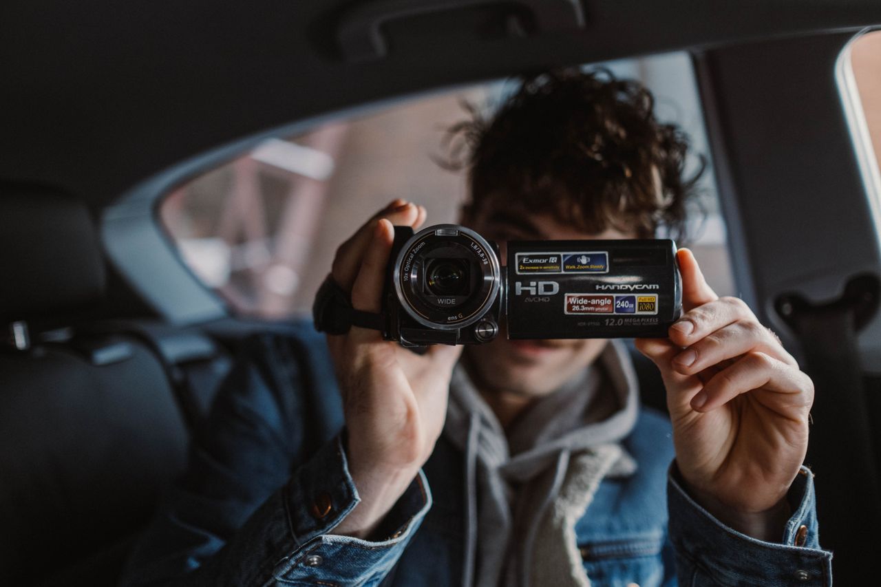 Person using a vintage camcorder inside a car, capturing moments through the lens.