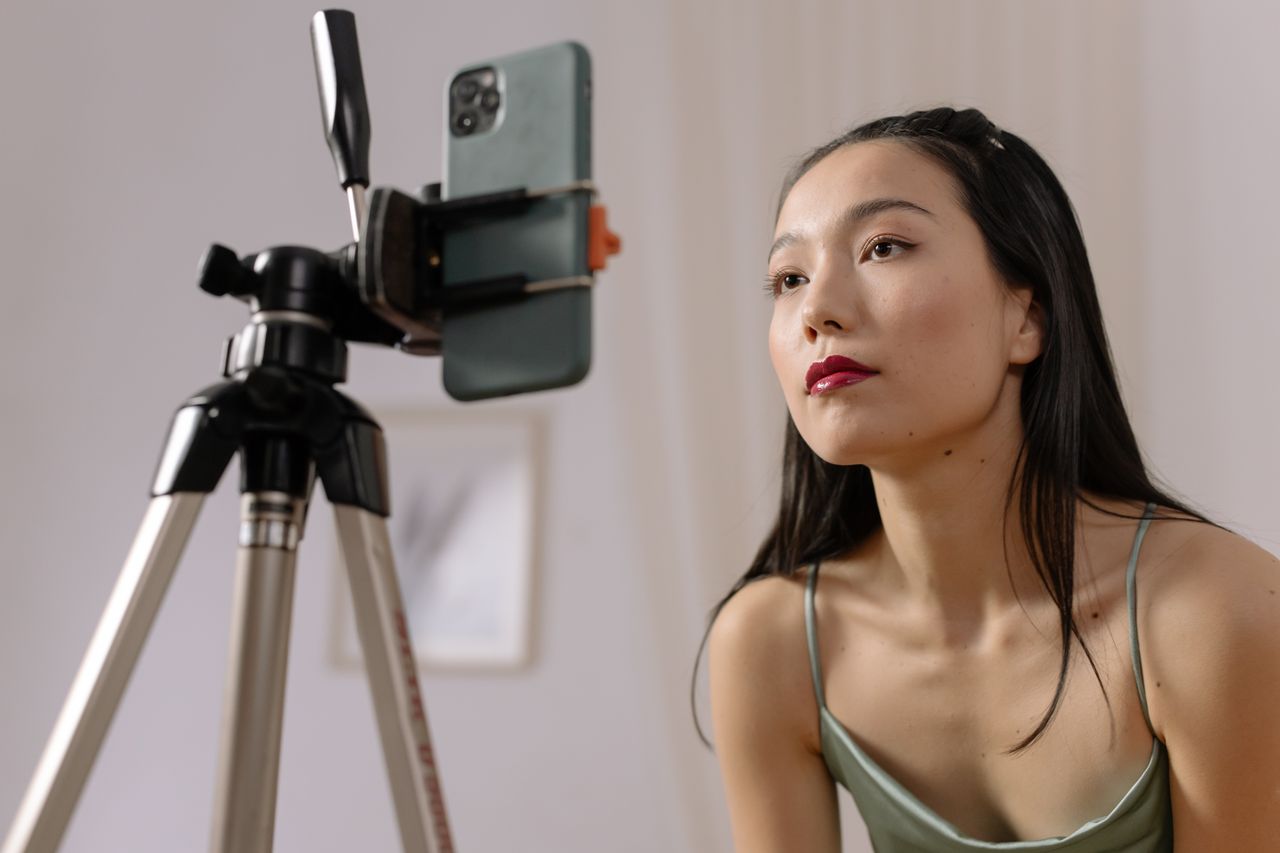about-02 Asian woman recording a vlog indoors using a smartphone on a tripod.