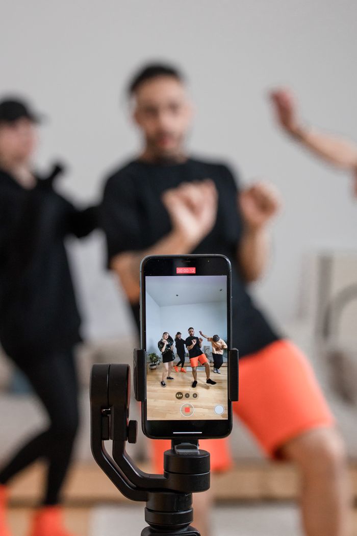 about-img A group of people recording a dance video using a smartphone indoors.